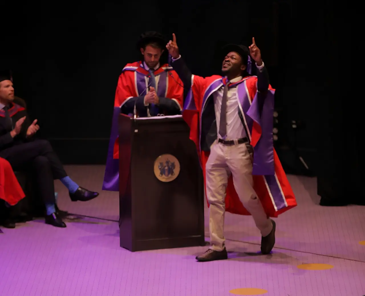 Prof. Andrew Agbaje raises his hands in celebration during PhD award ceremony, declaring 'To God be the glory.'